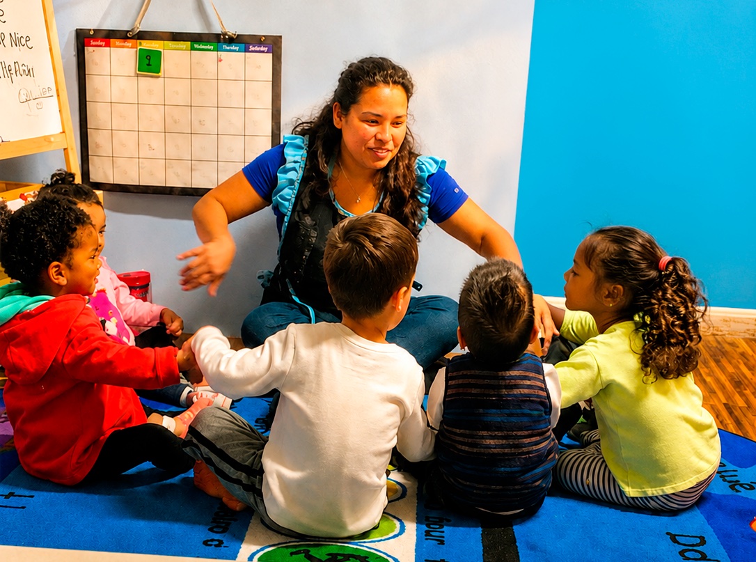 Sandra leading circle time with children seated together on a colorful learning rug